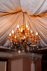 Beautiful crystal chandelier of yellow glass on the ceiling decorated with drapery.
