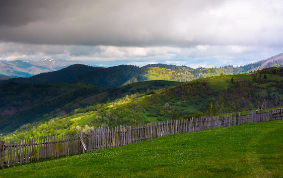 fence on the edge of the hillside. beautiful rural landscape of Carpathian mountains in springtime. forested hills under the heavy clouds in the distance