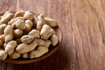 Unpeeled peanuts in wooden bowl over rustic wooden background closeup, selective focus