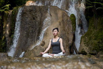 Young woman meditating in yoga pose near waterfall