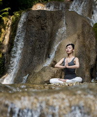 Young woman meditating in yoga pose near waterfall