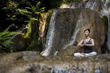 Young woman meditating in yoga pose near waterfall