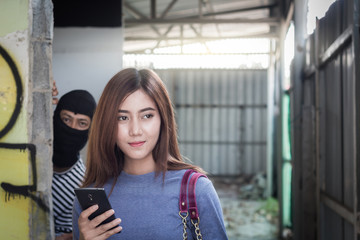 Beautiful young woman holding smartphone and being stalked by man criminal with the knife