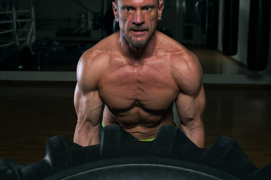 Functional training. Muscular strong man with naked troso lifting heavy tire.