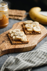 Two toasts with peanut paste, banana slices and chia seeds on a serving wooden board. The concept of healthy fitness breakfast.