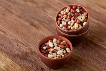Two ceramic bowls with raw peanuts mix isolated over rustic wooden backround, top view, close-up.