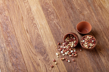 Obraz na płótnie Canvas Two ceramic bowls with raw peanuts mix isolated over rustic wooden backround, top view, close-up.