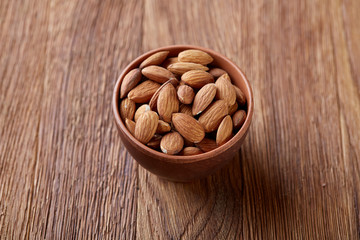 Bowl of almonds on wooden background, top view, close-up, selective focus.