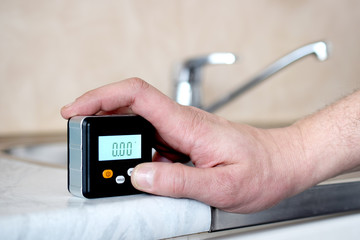 Man using a small digital spirit level to check level of kitchen sink table at home. 