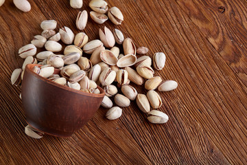 Overturned ceramic bowl with pistachious on wooden background, top view, selective focus.