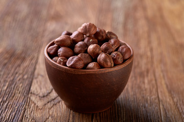 Hazelnuts in overturned ceramic bowl on wooden background with copy space, top view, selective focus.