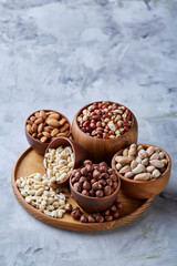 Mixed nuts in brown bowls on wooden tray over white background, close-up, top view, selective focus.