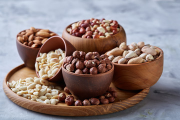 Mixed nuts in brown bowls on wooden tray over white background, close-up, top view, selective focus.