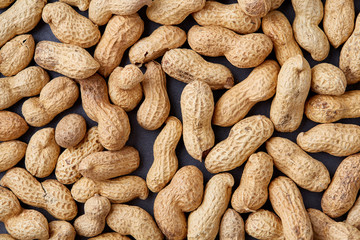 Unpeeled raw peanut on baking tray over white textured background, selective focus, shallow depth of field.