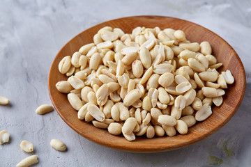 Peanuts in wooden plate isolated over white textured background, top view, close-up.
