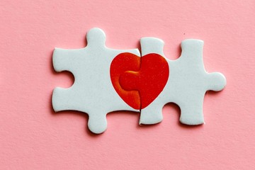closeup of two pieces of a puzzle with red heart on pink background
