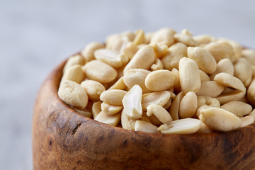 Peanuts in wooden plate isolated over white textured background, top view, close-up.
