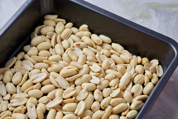 Peeled peanut on baking tray over white textured background, selective focus, shallow depth of field.