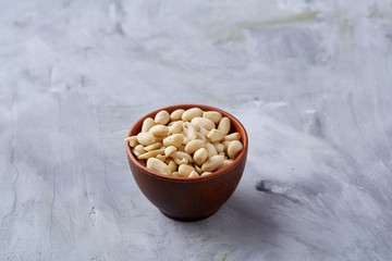 Peanuts in ceramic bowl isolated over white textured backround, top view, close-up.