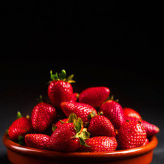 Strawberry. Fresh strawberry on black background with copy space for text. Heap of Red strewberry on a plate close up.
