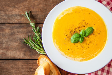 Cream soup with  Pumpkin and Carrot  on Red classic Checkered tablecloth on wooden rustic table. Squash Soup with herbs. Top view. Copy space.