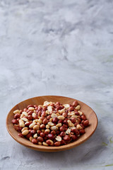 Raw mixed peanuts in wooden plate isolated over white textured background, top view, close-up.