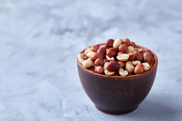 Raw mixed peanuts in wooden plate isolated over white textured background, top view, close-up.
