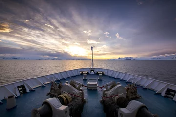 Foto op Canvas The bow of a ship appears as though it has sailed into a new world, as the spectacular sunset illuminates the sky over the mountains and glaciers of Antarctica. © Chris