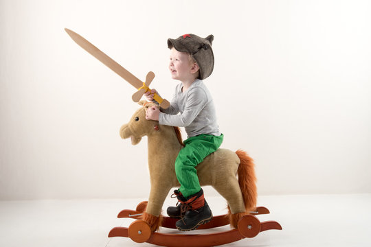 Funny child in old military cap with red star, on toy horse-rocking horse with wooden sword. Boy dreams of battles, victories and adventures. Concept training of spirit, education morale, patriotizm