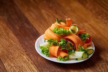 Artistically served vegetable salad with carrot, cucumber, letucce over wooden background, selective focus