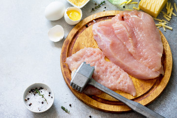 Preparing meat for cooking a turkey cutlet. Ingredients on a stone or slate table (turkey fillet, egg, cheese, corn flour, spices and olive oil). Copy space.