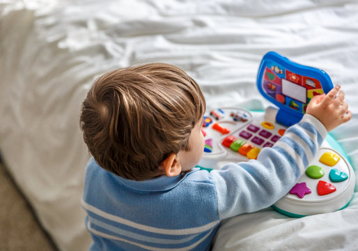 A boy plays with a musical toy on the bed of his room
