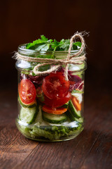 Delicious vegetable salad in jar and fresh veggies on cutting board on table, selective focus, close-up