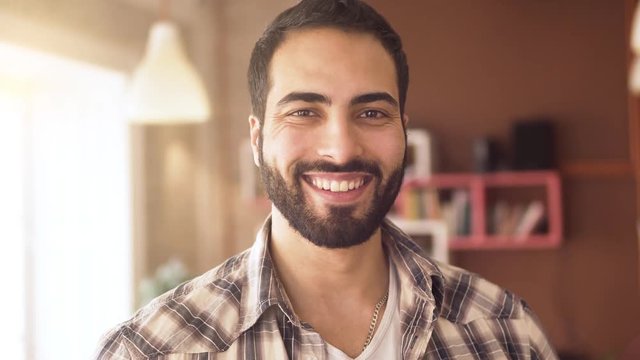 Smiling bearded man standing happily in light well-furnished room, portrait shot of handsome boy in checked shirt in day time