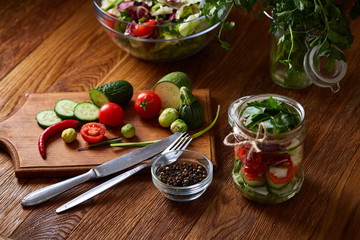 Delicious vegetable salad in jar and fresh veggies on cutting board on table, selective focus, close-up