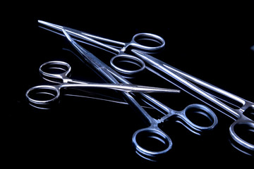 surgical instruments and tools including scalpels, forceps and tweezers on black mirror background.