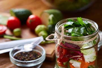 Delicious vegetable salad in jar and fresh veggies on cutting board on table, selective focus, close-up