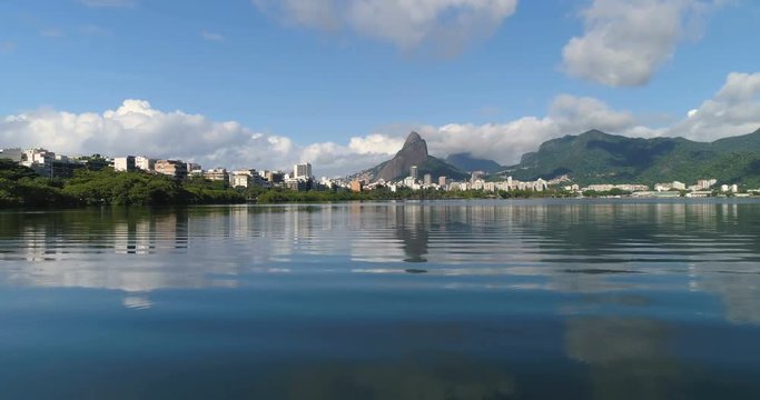 Flying low above water to reveal Rio de Janeiro city buildings. Water reflections
