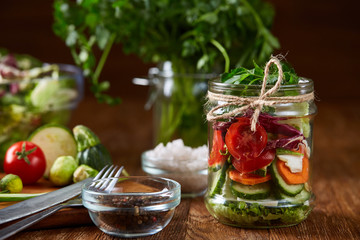 Delicious vegetable salad in jar and fresh veggies on cutting board on table, selective focus, close-up