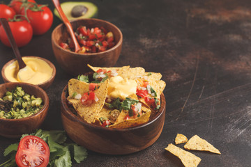 Mexican food concept. Nachos - yellow corn totopos chips with various sauces in wooden bowls: guacamole, cheese sauce, pico del gallo