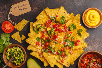 Mexican food concept. Nachos - yellow corn totopos chips with various sauces in wooden bowls: guacamole, cheese sauce, pico del gallo, top view