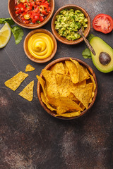 Mexican food concept. Nachos - yellow corn totopos chips with various sauces in wooden bowls: guacamole, cheese sauce, pico del gallo, copy space, top view