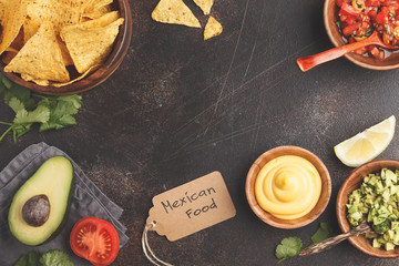 Mexican food concept. Nachos - yellow corn totopos chips with various sauces in wooden bowls: guacamole, cheese sauce, pico del gallo, frame of food, top view, copy space.