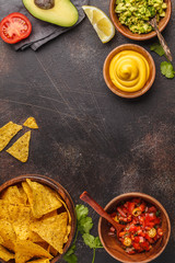 Mexican food concept. Nachos - yellow corn totopos chips with various sauces in wooden bowls: guacamole, cheese sauce and tomato sauce, frame of food, top view, copy space.