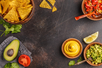 Mexican food concept. Nachos - yellow corn totopos chips with various sauces in wooden bowls: guacamole, cheese sauce, pico del gallo, frame of food, top view, copy space.