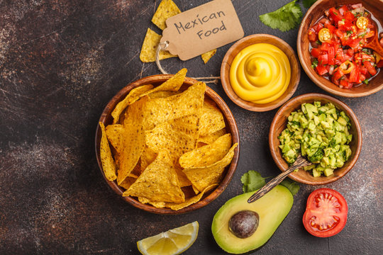 Mexican food concept. Nachos - yellow corn totopos chips with various sauces in wooden bowls: guacamole, cheese sauce, pico del gallo, copy space, top view