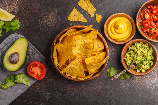 Mexican food concept. Nachos - yellow corn totopos chips with various sauces in wooden bowls: guacamole, cheese sauce and tomato sauce, copy space, top view