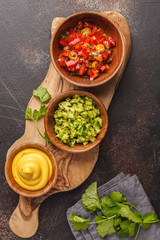 Mexican food concept. Various sauces to nachos or tacos in wooden bowls: guacamole, cheese sauce, pico del gallo. Top view, copy space