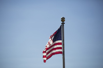 American flag waving vigorously in the wind against a blue sky