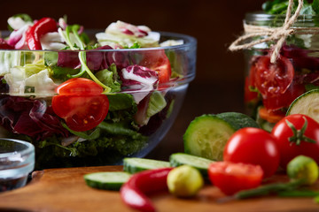 Delicious vegetable salad in jar and fresh veggies on cutting board on table, selective focus, close-up